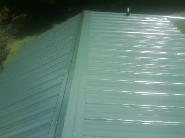 New green metal panels meeting at the ridge of a roof — Flat Roof Repair work by our crew in Lewiston